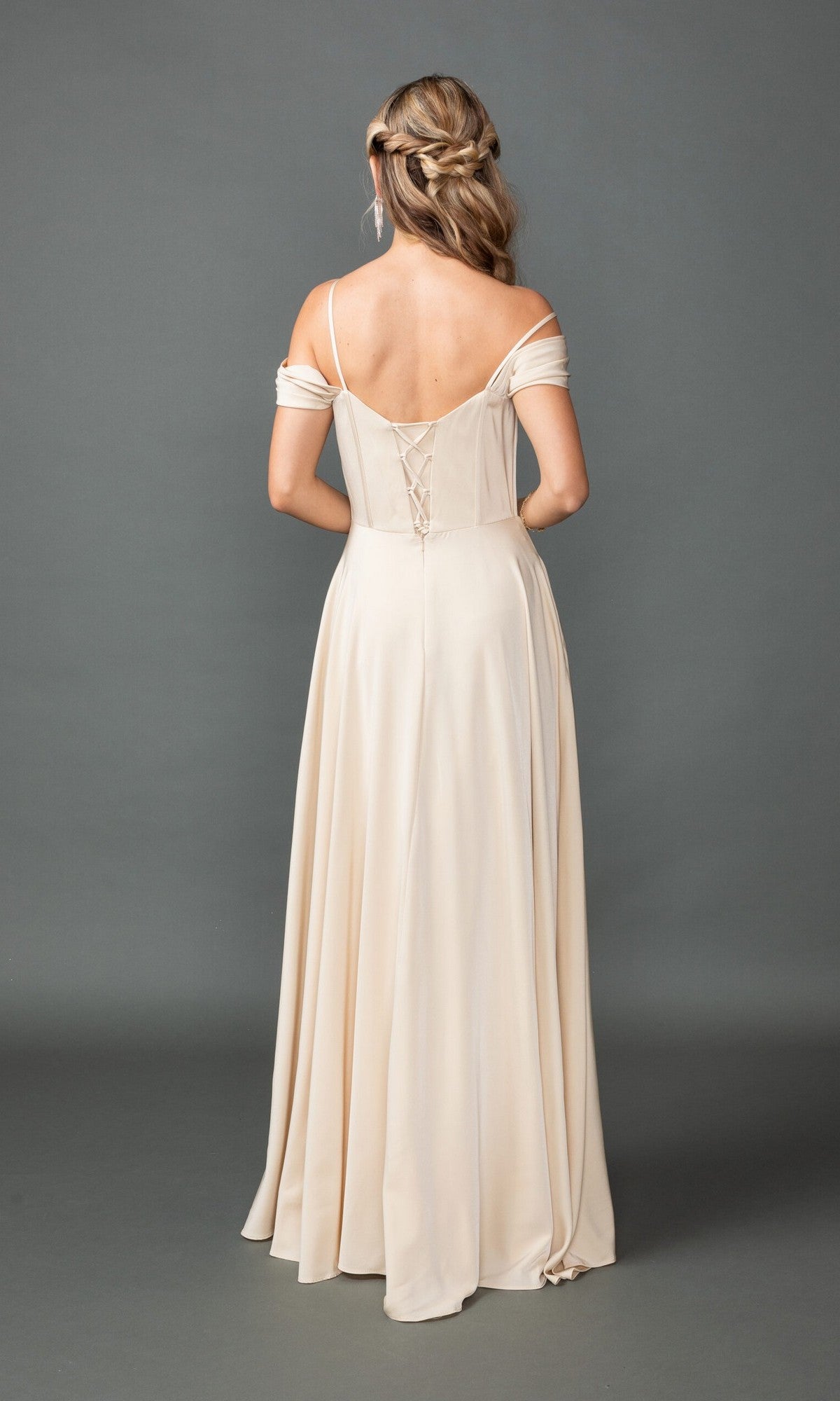A woman faces away, wearing the Dancing Queen 4539 long prom dress—a cream, off-shoulder A-line gown with a corset bodice and lace-up back. Her hair is styled in loose waves and braids.